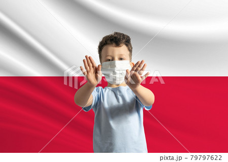 Little white boy in a protective mask on the background of the flag of Poland. Makes a stop sign with his hands, stay at home Poland 79797622
