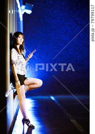 雨の夜中でスマホ片手に夜遊びの待ち合わせをする女の子 79799117