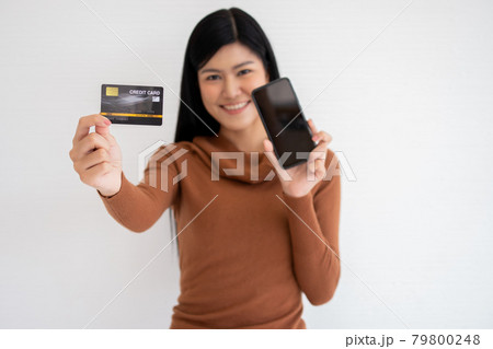 Happy Asian woman holding card credit and smartphone for mobile banking on the internet. Concept of new lifestyle and financing technology. Happy Asian woman holding card credit and smartphone for mobile banking on the internet. Concept of new lifestyle and financing technology. 79800248