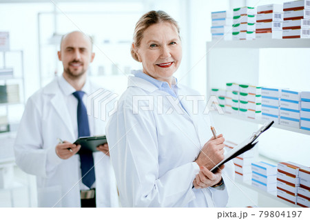 pharmacist with a clipboard and her colleague standing near a pharmacy display case . 79804197