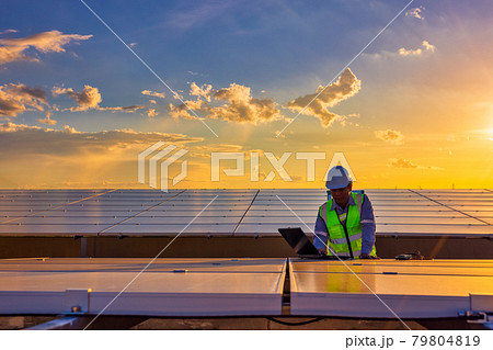 Engineer using laptop at solar panels on rooftop at sunset sky, An engineer working at a photovoltaic farm. Eco technology for electric power 79804819