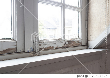 Old wooden window frames with rotting wood and cracked peeling paint, house needs renovation and new frames 79807297