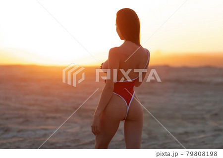 Alluring young woman covering naked breast while standing in sandy desert valley at sundown Alluring young woman covering naked breast while standing in sandy desert valley at sundown 79808198