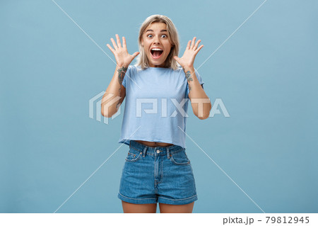You gotta listen this. Thrilled amused and amazed impressed good-looking young european female with blond hair gasping holding breath and smiling broadly raising palms from surprise over blue wall 79812945