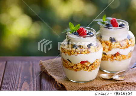 granola with greek yogurt and berries in two glass jars 79816354