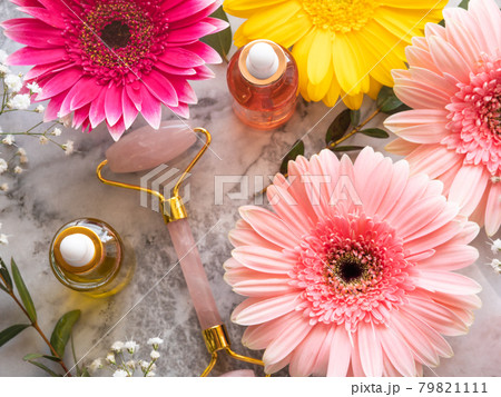 Pink quartz face roller gua sha and serum in bottle on marble table. Skin care concept with flowers 79821111