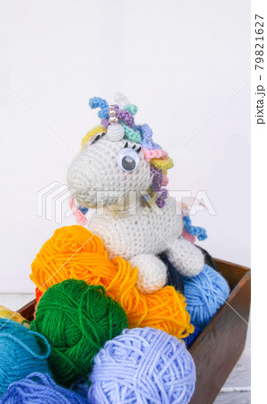 Handmade crocheted unicorn toy and yarn in a wooden box on white background. 79821627