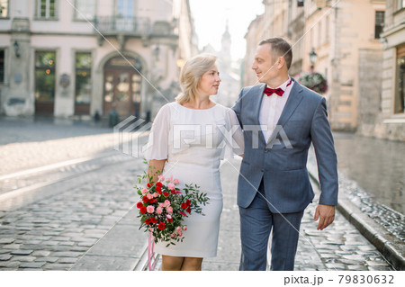 Mature couple in elegant fashionable clothes, walking in the street of old European city Mature couple in elegant fashionable clothes, walking in the street of old European city 79830632