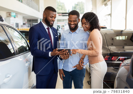Dealership Center Manager Showing Vehicle Characteristics On Digital Tablet To Black Couple Dealership Center Manager Showing Vehicle Characteristics On Digital Tablet To Black Couple 79831840