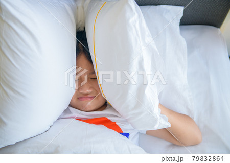 Little girl lying in bed covering head with pillow because too loud annoying noise Little girl lying in bed covering head with pillow because too loud annoying noise 79832864