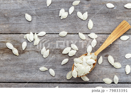 Pumpkin seeds in a wooden spoon and scattered on a wooden table. Pumpkin seeds in a wooden spoon and scattered on a wooden table. 79833391