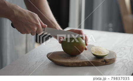 Man cutting ripe mango on olive board on white oak table 79837035