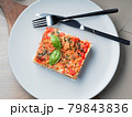 Piece of lasagna. White plate with fork and knife 79843836