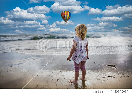 Blond child looking at the sea with blue sky and balloon. Blond child looking at the sea with blue sky and balloon. 79844044