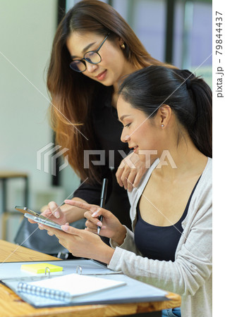 Portrait of two female friends using their mobile phone 79844437