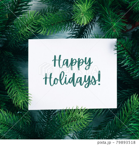 Christmas new year background with white card with text wishing Happy Holidays in green branches Christmas new year background with white card with text wishing Happy Holidays in green branches 79893518