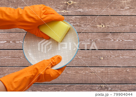 Women's hands in protective glove with sponge and plate on wooden background. Women's hands in protective glove with sponge and plate on wooden background. 79904044