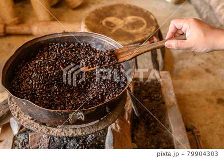 Cropped shot view of woman hill tribe hand trying to roasting coffee beans by traditional local ways, using metal pot and wooden spatula. Roasting brings out the aroma and flavor inside coffee beans. 79904303