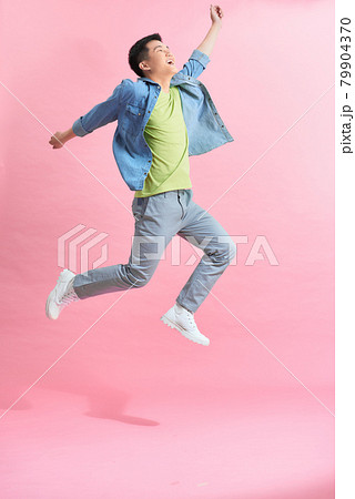 Fun energetic Asian man jumping in mid air isolated on light pink background 79904370