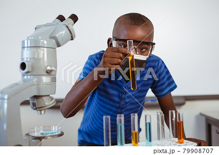 African american schoolboy in safety glasses and face mask looking at test tubes in science class 79908707