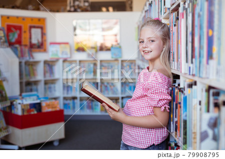 Portrait of smiling caucasian schoolgirl standing reading book in school library Portrait of smiling caucasian schoolgirl standing reading book in school library 79908795