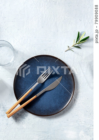 Blue ceramic plate, shot from the above with cutlery and an olive branch 79909088