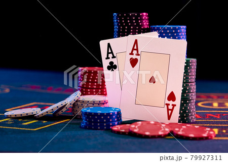Two aces standing leaning on chips piles, some of them are laying nearby on blue cover of playing table. Black background. Casino concept. Close-up. 79927311