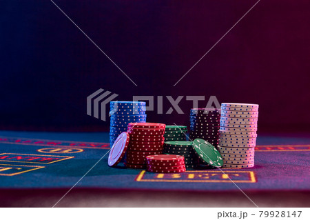 Colorful chips piles standing on blue cover of playing table. Black background. Gambling entertainment, poker, casino concept. Close-up. Colorful chips piles standing on blue cover of playing table. Black background. Gambling entertainment, poker, casino concept. Close-up. 79928147