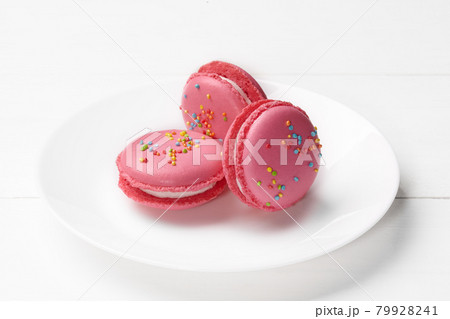 Three pink macarons with creamy fillings and sprinkles on plate 79928241