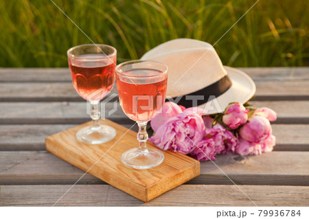 two glasses with rose wine and pink peony bouquet. delicious refreshing drink, huge blossoming flowers and mens hat two glasses with rose wine and pink peony bouquet. delicious refreshing drink, huge blossoming flowers and mens hat 79936784
