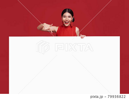 Happy asian woman in red casual attire with hand pointing blank announcement banner in red background. Happy asian woman in red casual attire with hand pointing blank announcement banner in red background. 79936822