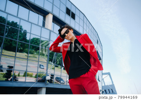 A girl in a red suit stands against the background of a modern building in the city 79944169