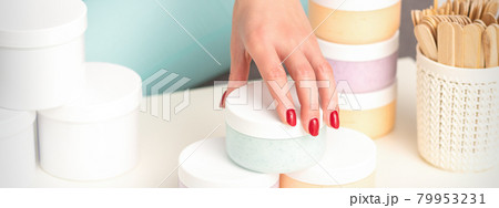 Beautician's hand takes jar with cosmetics from table offering and selling cosmetic products, moisturizing cream, wax paste. 79953231