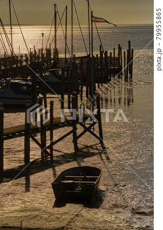 Port with a wooden ship mooring in the Wadden Sea of the North Sea at sunrise with a rowing boat on the beach 79955865