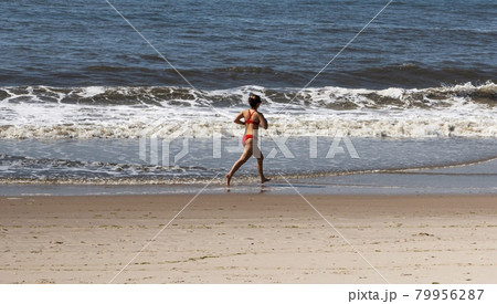 Female lifeguard in red bikini running in the ocean water on the edge of the beach 79956287