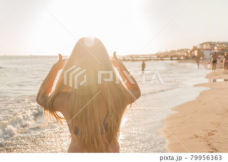 Young girl straightens her hair with her hands against the backdrop of the sea beach and sunset 79956363