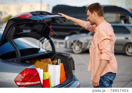 Man puts his purchases in the trunk on parking 79957403