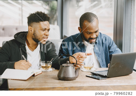 Two men sitting in a cafe and working behind a laptop and drink a tea. 79960282