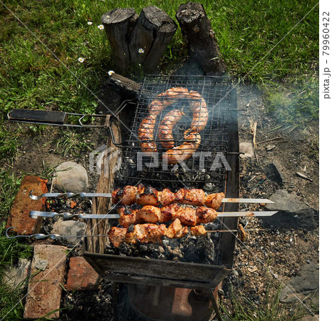 Barbeque meat and sausages or bratwurst on a grill grate in backyard. Man preparing shashlik or shish kebab over charcoal. Grilled meat on metal skewer outdoor. BBQ party or picnic food. Close up shot 79960422
