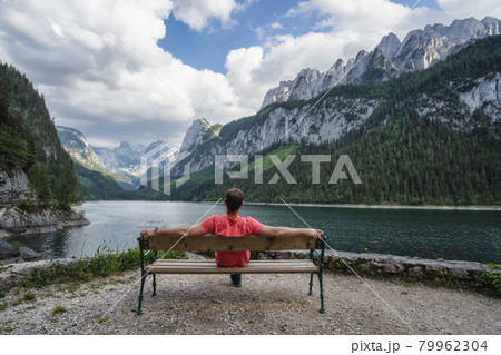 Man relaxing on bench in front of Dachstein Mountains reflected in Gosau lake, Austria Man relaxing on bench in front of Dachstein Mountains reflected in Gosau lake, Austria 79962304