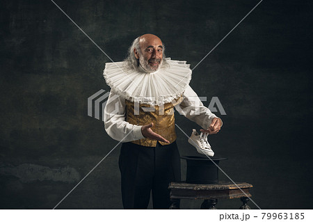 Elderly gray-haired man, actor or magician isolated on dark vintage background. Retro style, comparison of eras concept. 79963185