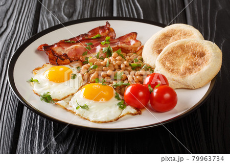 Delicious breakfast of fried eggs, beans, bacon, tomatoes and English muffins close-up in a plate. horizontal Delicious breakfast of fried eggs, beans, bacon, tomatoes and English muffins close-up in a plate. horizontal 79963734
