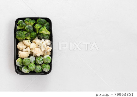 Frozen vegetables in a plastic container on a white background. Set of cabbage, broccoli, cauliflower, brussels sprouts. View from above. Copy space. 79963851