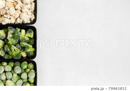 Border of frozen vegetables in plastic containers on a white background. Cabbage mix. Brussels sprouts, broccoli, cauliflower. Space for text. Top view, flat lay. 79963852