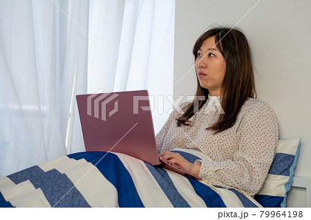 ベッドの中でノートパソコンを開く女性 79964198