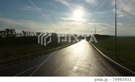 Drone rises above wet asphalt road for cars between sown fields Drone rises above wet asphalt road for cars between sown fields 79965931