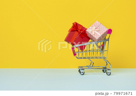 Toy shopping cart or trolley with full with gift boxes. A gift for a holiday, anniversary or birthday. Trolley cart with gift boxes Isolated over yellow background 79971671