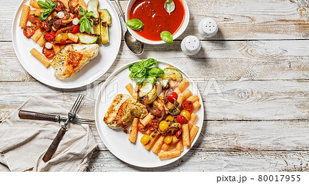 Food banner. Grilled turkey fillet, penne pasta with tomatoes, spices, Parmesan cheese and fresh basil. Tomato sauce. Traditional Italian cuisine. Two servings on a wooden background. Copy space Food banner. Grilled turkey fillet, penne pasta with tomatoes, spices, Parmesan cheese and fresh basil. Tomato sauce. Traditional Italian cuisine. Two servings on a wooden background. Copy space 80017955