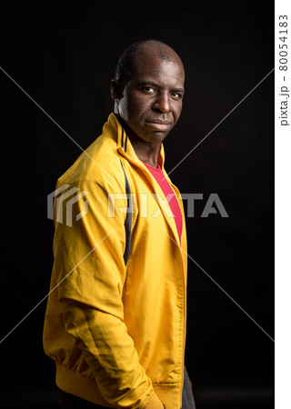 Side view of an African American man standing looking at camera black background Side view of an African American man standing looking at camera black background 80054183