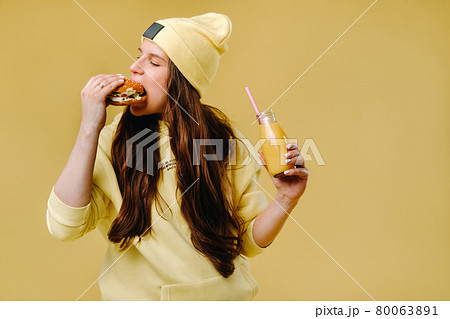 pregnant girl in yellow clothes with hamburgers in her hands on a yellow background pregnant girl in yellow clothes with hamburgers in her hands on a yellow background 80063891
